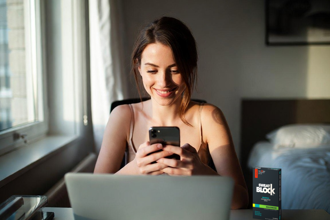 A creator using her phone beside a laptop.